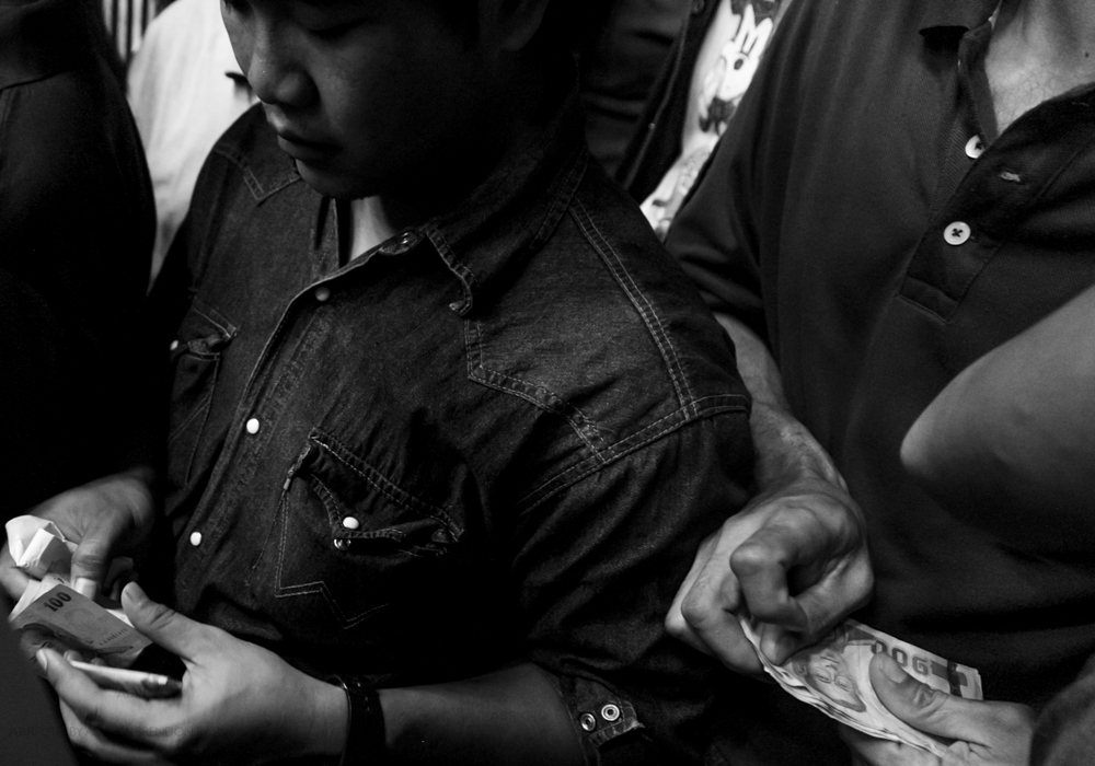 Men who have placed bets on the fight count their winnings during a Muay Thai fight at Chang 7